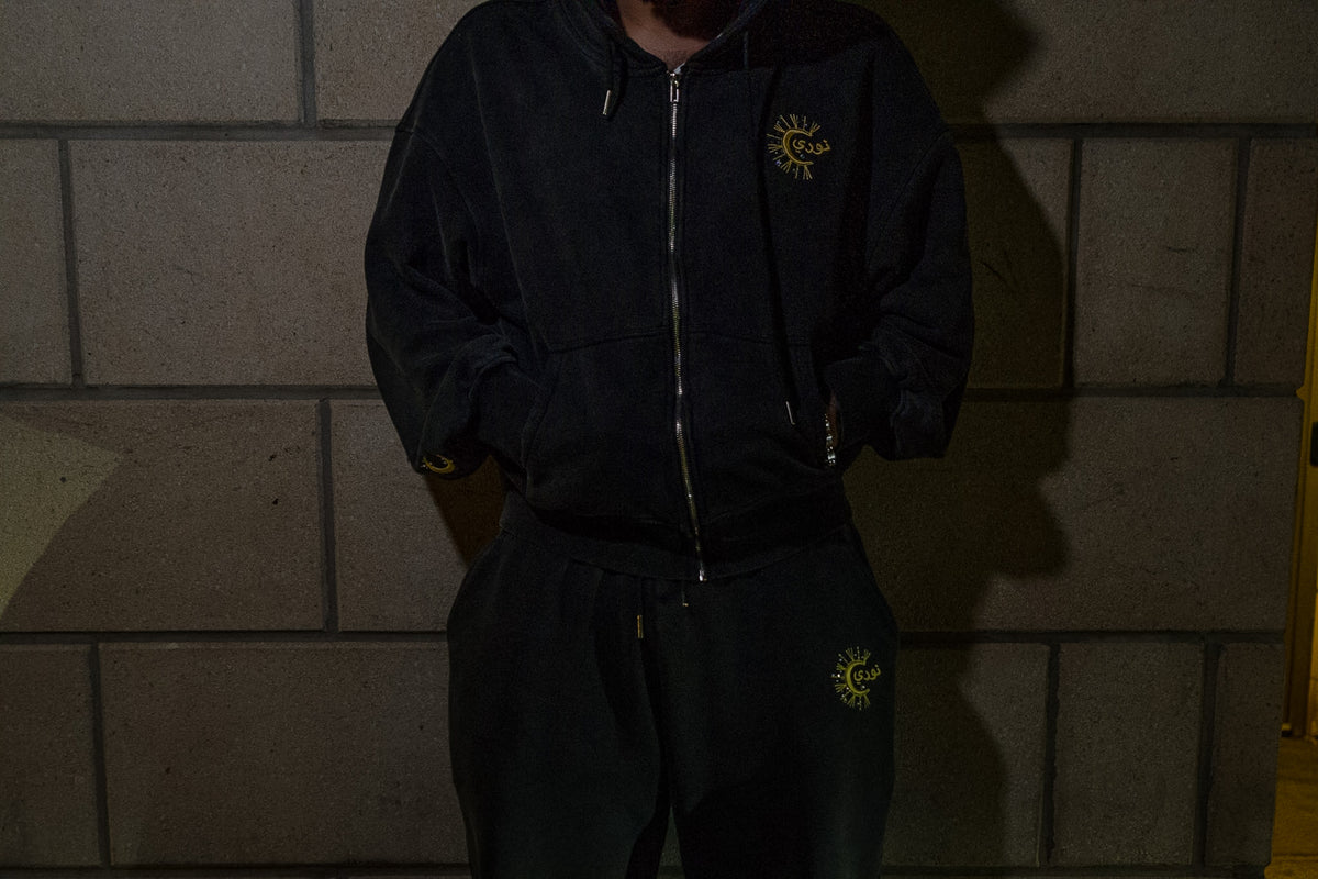 The Dawn zip-up and flared sweatpant worn against a wall at night