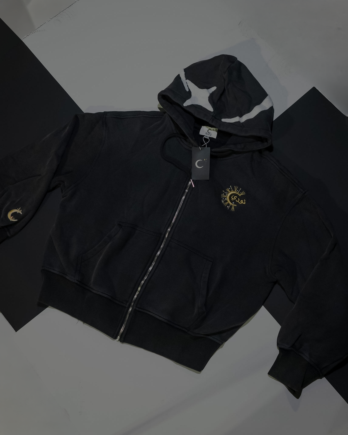 The Dawn zip-up hoodie laid flat, star appliqué on the hood, gold نوري embroidery at the chest